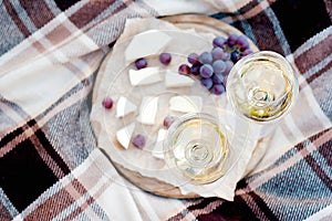 Two glasses of white wine and a wooden plate with cheese and grapes served outside