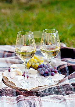 Two glasses of white wine and a wooden plate with cheese and grapes served outside