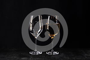 Two glasses for wine on a black background. One empty, the second half full of white wine.