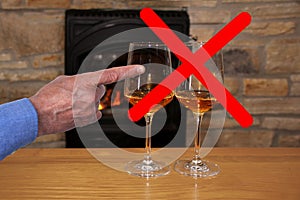 Two glasses of wine in front of the fireplace crossed out with a red cross, a male hand shows the concept of giving up alcohol