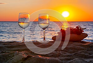 Two glasses of wine and grapes on sandy beach at sunset, Sicily island, Italy