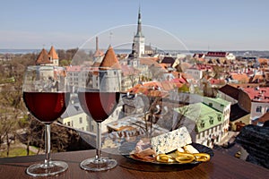 Two glasses of wine with mixed snacks against view from above of historic old town in Tallinn. Glass of red wine with different