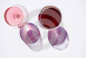Two glasses of wine: red and pink on white background with sparkling shadows. Top view. Free copy space.