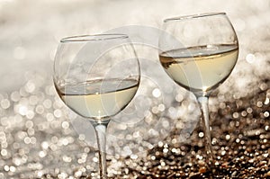 Two glasses of wine on the seashore in the waves and sparkling bokeh