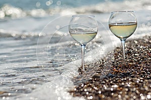 Two glasses of wine on the seashore in the waves and sparkling bokeh
