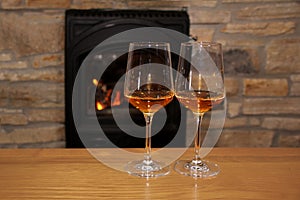 Two glasses of wine standing on a table in front of a fireplace in which firewood burns with a bright flame, a concept of a