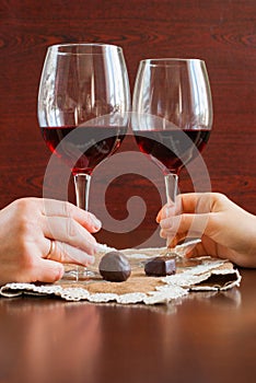 Two glasses of wine on a wooden table. Candies. Hands.