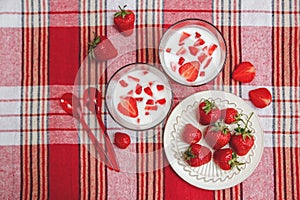 Two Glasses of Yogurt,Red Fresh Strawberries are in the Ceramic Plate with Plastic Spoons on the Check Tablecloth.Breakfast Organi
