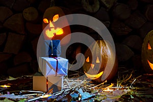 Two glowing pumpkins and gifts on halloween night with candles on a background of firewood and autumn foliage