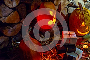 Two glowing pumpkins and gifts on halloween night with candles on a background of firewood and autumn foliage