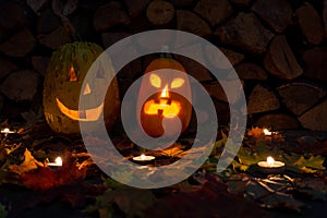 Two glowing pumpkins on halloween night with candles on a background of firewood and autumn foliage