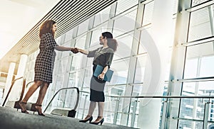 Two go getters coming together. Low angle shot of two attractive young businesswomen shaking hands while standing in a