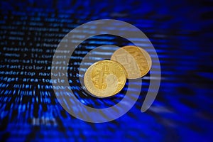 Two gold bitcoin coins on the background of lines of program code