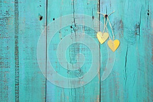 Two gold hearts hanging on antique teal blue wood fence