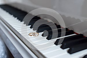 Two gold rings lie on the keys of white piano