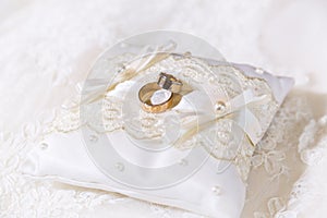 Two gold shiny wedding rings together on satin lace pillow