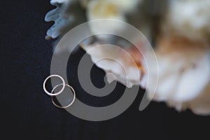 Two gold wedding rings with a diamond on a black background with a wedding bouquet