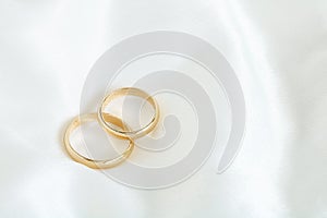 Two gold wedding rings on a white satin.