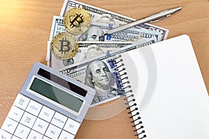 Two golden bitcoins, journal, pen, and calculator on us dollars
