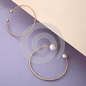 Two golden bracelets with pearls on beige and purple background with copy space