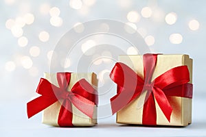 Two golden gift box or present box with red ribbon against holiday lights background for Christmas greeting