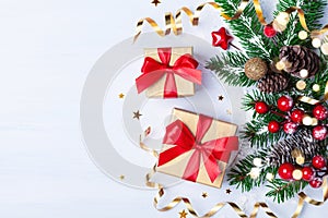 Two golden gift or present boxes, snowy fir branches, conifer cones, Christmas decoration and red berry on white table top view