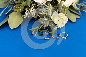 Two golden wedding rings and engagement ring with a diamond on blue background