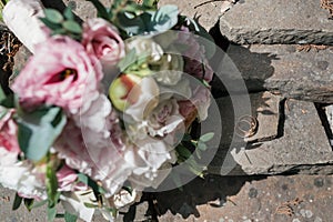 Two golden wedding rings on stone near   beautiful wedding bouquet of white and pink peony and roses in blur outdoors, close up.