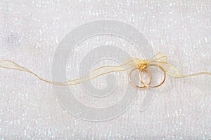 Two golden wedding rings tied with a golden ribbon on white shiny background