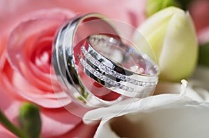 Two golden wedding rings white gold laying in the Bridal Bouquet on beautiful pink rose flower background.