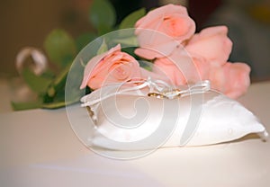 Golden wedding rings on a white pad near pink roses bouquet