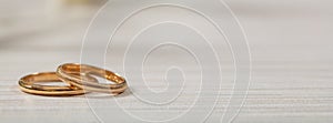 Two golden wedding rings on white wooden background, banner, copy space