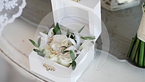 Two golden wedding rings in a white wooden box with rose flowers