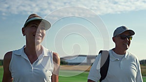 Two golf players walk country club course. Smiling couple talking sport outside.