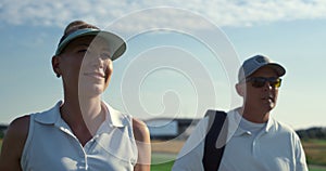 Two golf players walk country club course. Smiling couple talking sport outside.