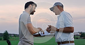 Two golfers communicate outside on sunset fairway. Golf group talk in sportswear