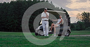 Two golfers rest outdoors on golf course. Married couple relax in golf cart.