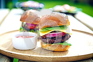 Two gourmet burgers with sauce on the side outdoors.