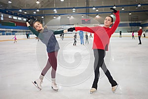 Two graceful girls pose on skate in indoor ice photo