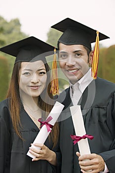 Two graduates holding diplomas outside portrait