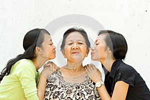 Two granddaughter kiss their old grandmother
