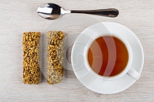 Two granola bar, tea in cup on saucer, teaspoon