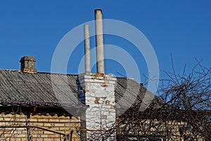 Two gray pipes on a brick chimney on a gray slate roof of a rural house