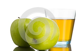 Two green apples next to a glass of apple juice
