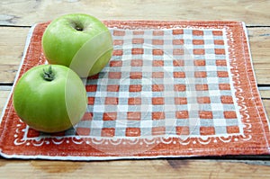 Two green apples on an orange napkin.