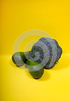 Two green avacados and broccoli on a yellow background