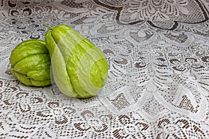 Two green chayotes on a table with a fine brown knitted tablecloth