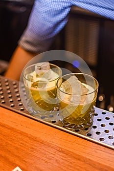 two green cocktails in rocks glasses on the edge of a bar