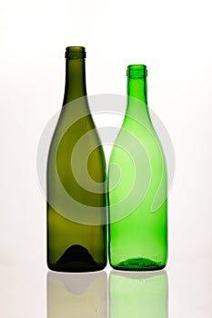 two green and empty wine bottles of different sizes and forms and their reflections