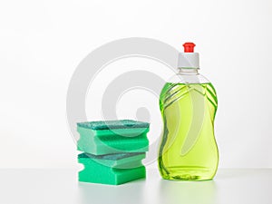 Two green foam sponges and dish washing gel on a white table.